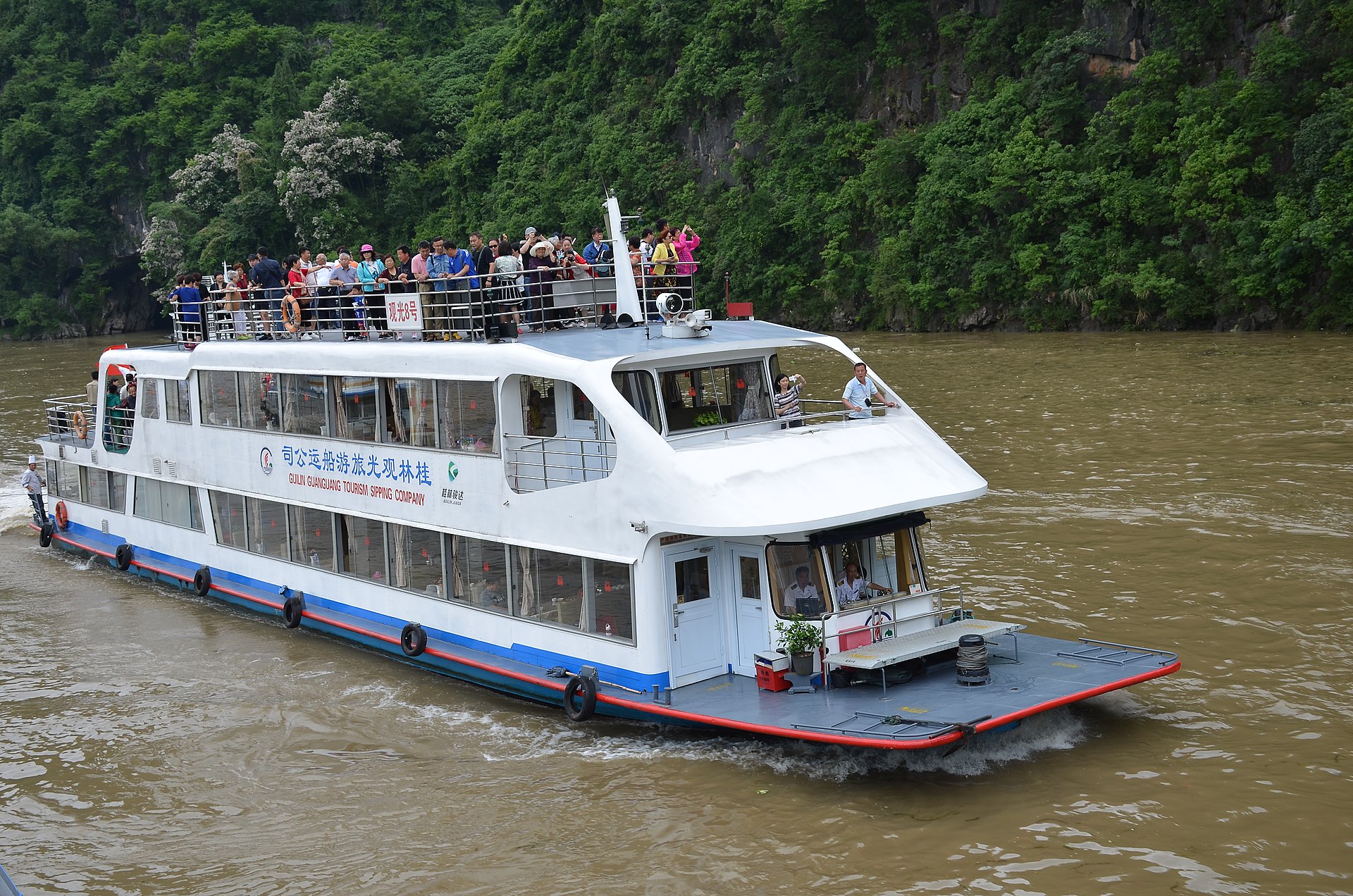 A multideck Guilin sightseeing boat carrying passengers on the Li River beside green karst slopes in 2017.
