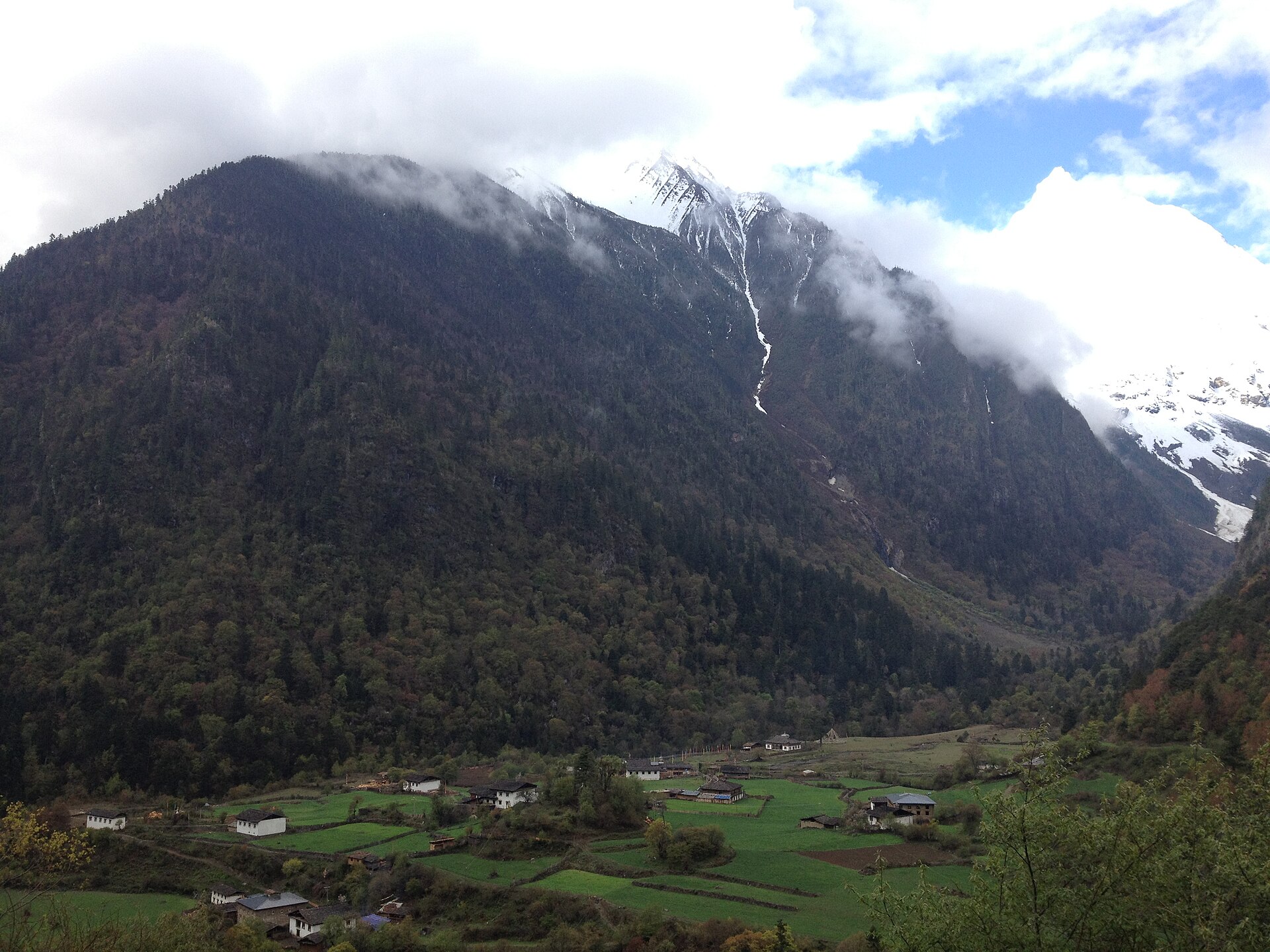 Yubeng Village in Deqin County beneath forested slopes and snow-covered Meili mountains.